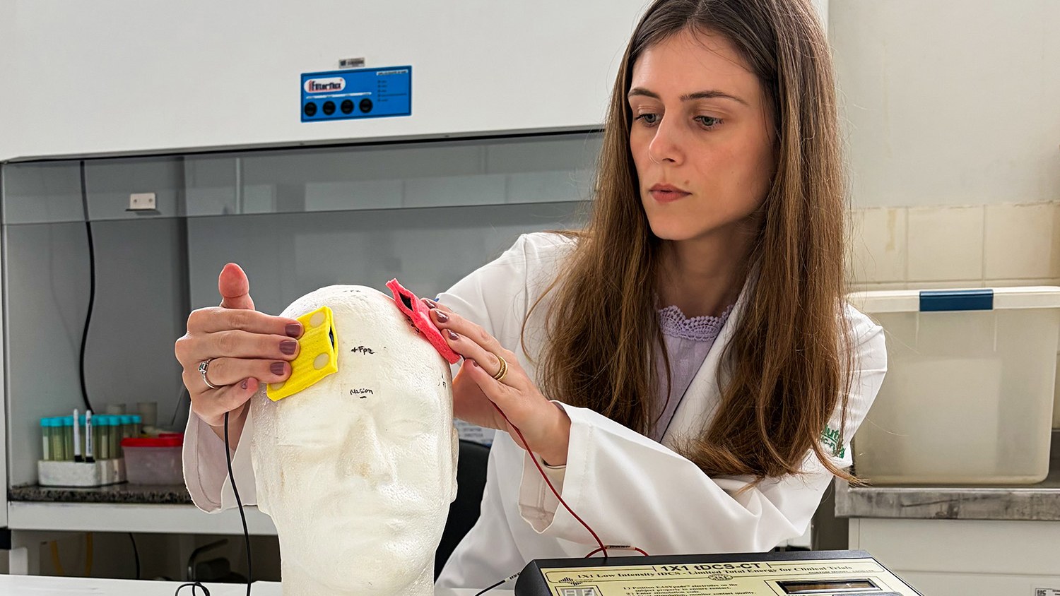 Investigadora coloca los electrodos de estimulación transcraniana sobre un modelo de cabeza en un laboratorio de la USP